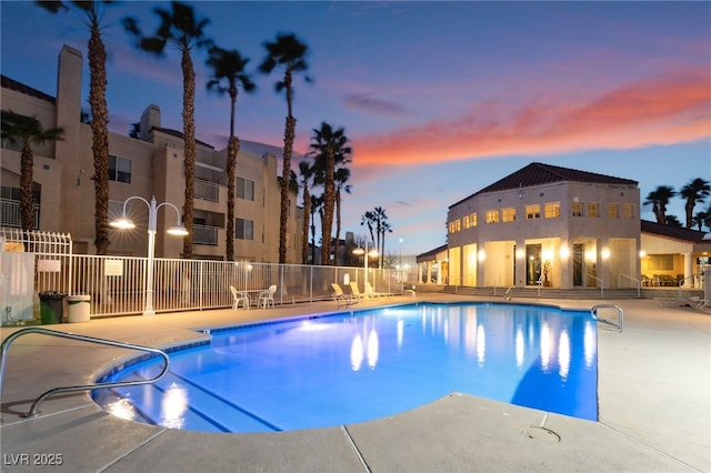 pool at dusk with a patio, a community pool, and fence