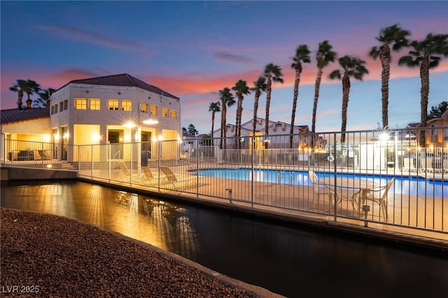 pool at dusk featuring a community pool and fence