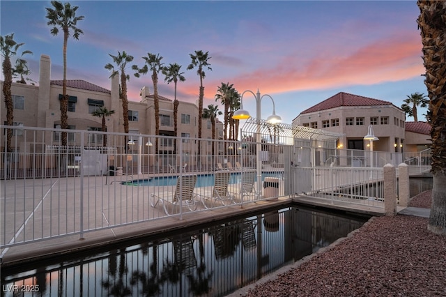 pool at dusk featuring a community pool and fence