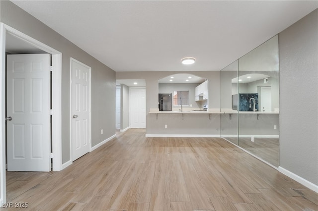 unfurnished living room featuring light wood-type flooring, baseboards, and arched walkways