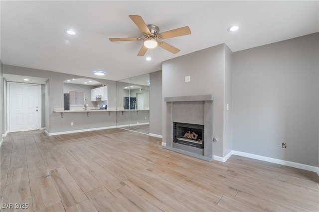 unfurnished living room featuring a fireplace, light wood-style floors, baseboards, and a ceiling fan