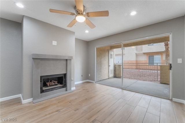 unfurnished living room with ceiling fan, a fireplace, baseboards, and wood finished floors