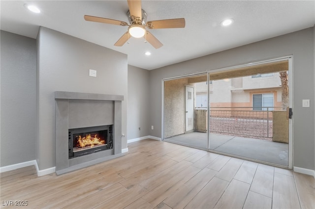 unfurnished living room with ceiling fan, baseboards, a lit fireplace, and wood finished floors