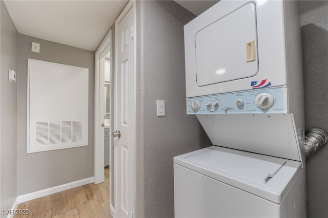 clothes washing area with stacked washer / dryer, baseboards, laundry area, light wood-style flooring, and a textured wall