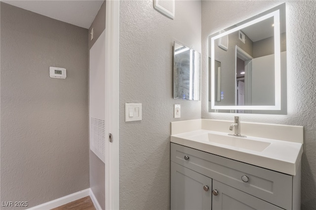 bathroom with visible vents, baseboards, a textured wall, wood finished floors, and vanity