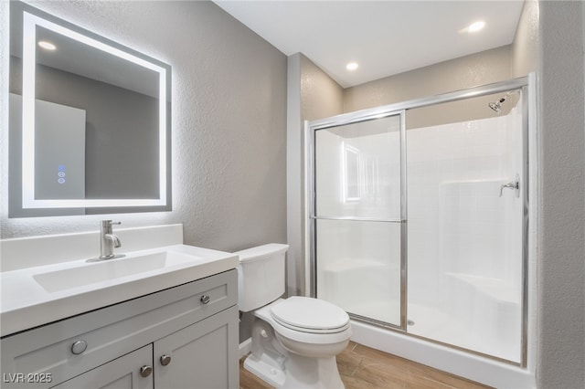 bathroom with toilet, a stall shower, wood finished floors, vanity, and a textured wall