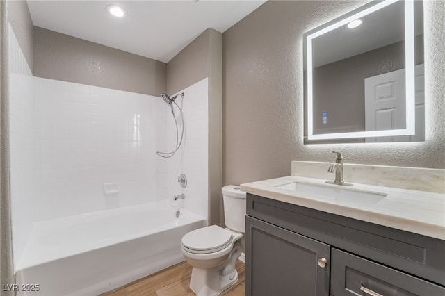 full bath with toilet, shower / tub combination, wood finished floors, vanity, and a textured wall