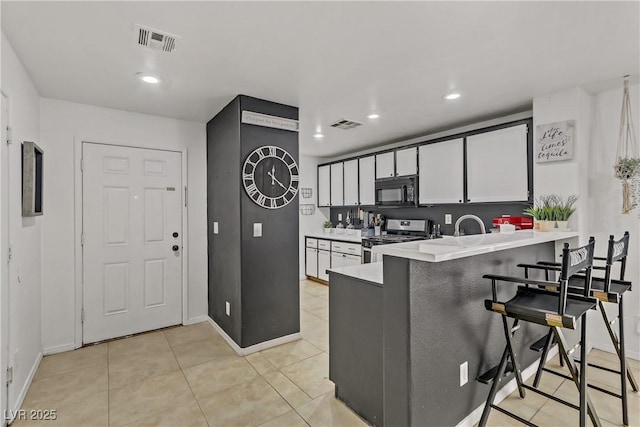 kitchen featuring visible vents, black microwave, stainless steel range with gas stovetop, a kitchen bar, and a peninsula