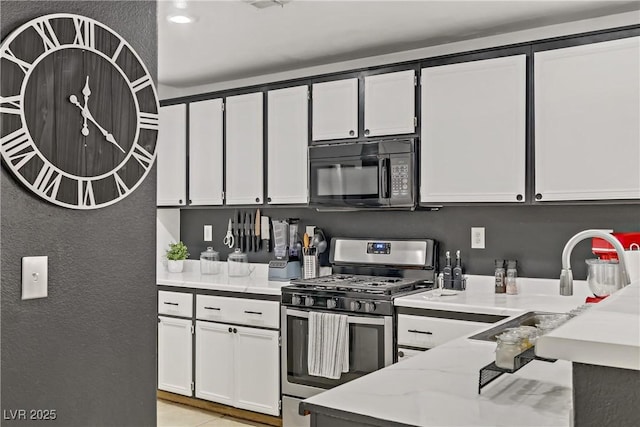 kitchen with light stone countertops, gas stove, a sink, white cabinets, and black microwave