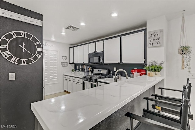 kitchen featuring visible vents, black microwave, gas range, light stone counters, and recessed lighting