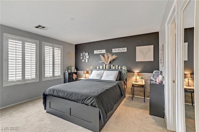 carpeted bedroom featuring an accent wall, visible vents, and baseboards