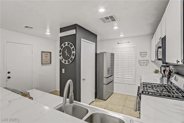 kitchen featuring light stone counters, stainless steel appliances, visible vents, and white cabinets