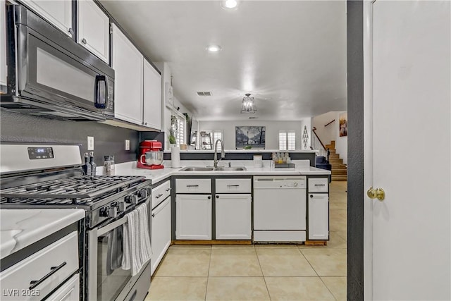 kitchen with stainless steel gas range, a peninsula, white dishwasher, a sink, and black microwave