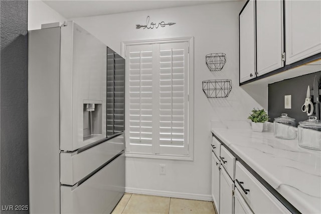 kitchen with light tile patterned floors, stainless steel fridge, white cabinets, and light stone countertops