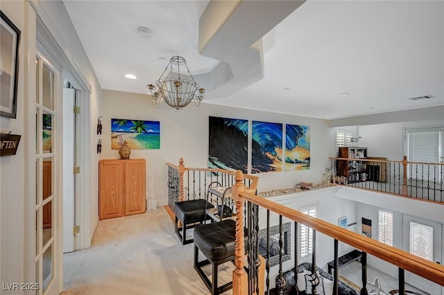 hall with a notable chandelier, an upstairs landing, light colored carpet, and a wealth of natural light