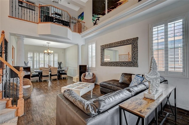 living room with wood finished floors, stairs, an inviting chandelier, and decorative columns