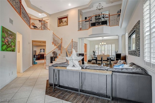 living room featuring visible vents, baseboards, stairway, decorative columns, and a notable chandelier