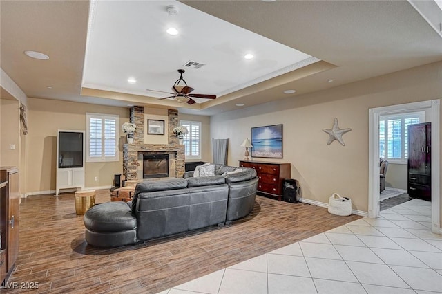 living area featuring light tile patterned floors, visible vents, a fireplace, and a tray ceiling