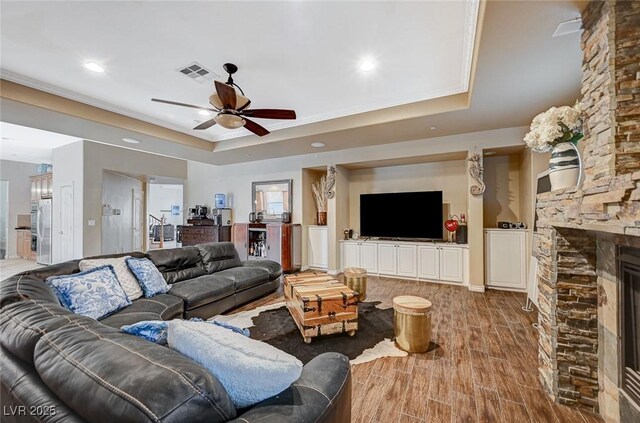 living room with visible vents, a fireplace, wood finished floors, a raised ceiling, and a ceiling fan