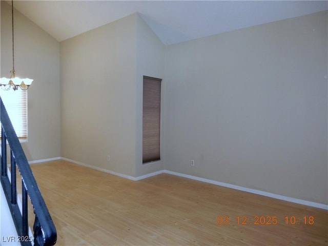 empty room with baseboards, a notable chandelier, light wood-style flooring, and vaulted ceiling