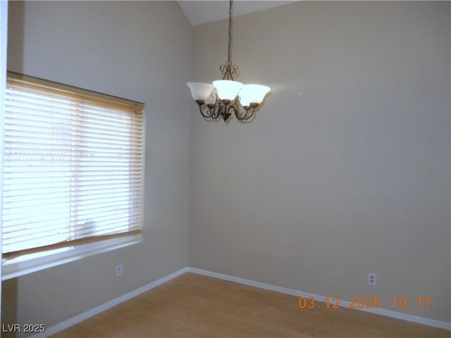 empty room featuring baseboards, an inviting chandelier, light wood-style flooring, and vaulted ceiling