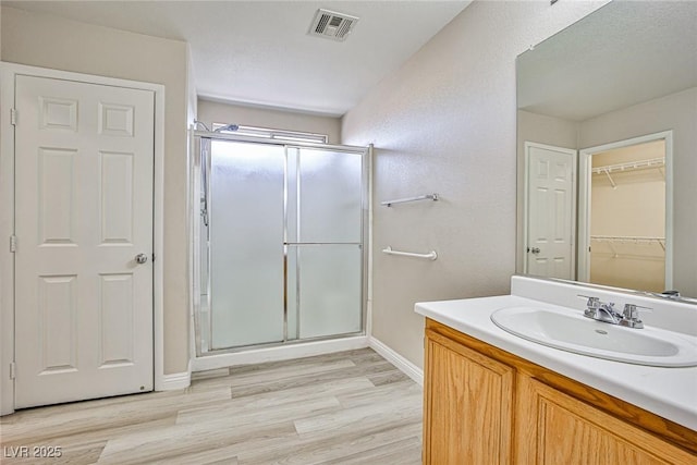 full bath with vanity, a shower stall, wood finished floors, and visible vents