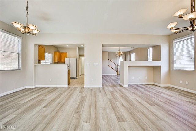 unfurnished living room with a chandelier, baseboards, stairs, and light wood-style floors