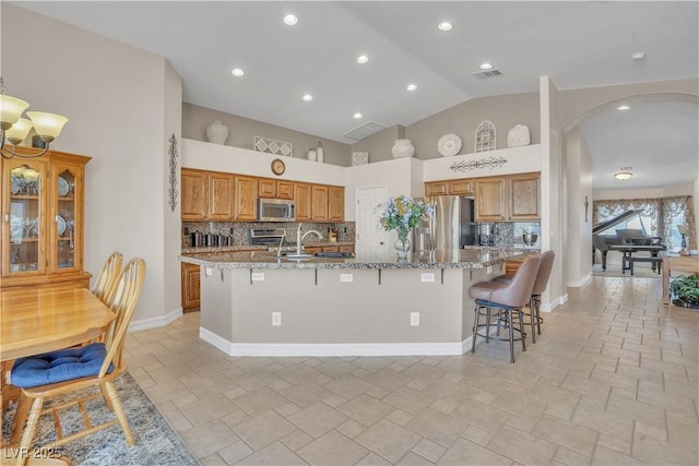 kitchen with backsplash, light stone countertops, a breakfast bar, a large island, and stainless steel appliances