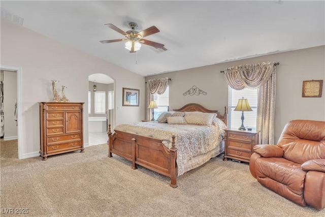 bedroom featuring visible vents, lofted ceiling, arched walkways, ensuite bathroom, and light carpet