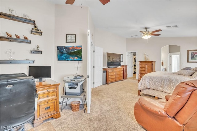 bedroom with visible vents, arched walkways, ceiling fan, a walk in closet, and light colored carpet