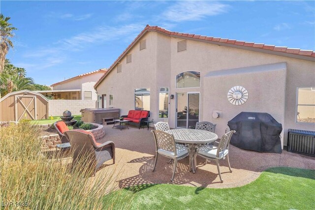 back of house with a hot tub, stucco siding, an outbuilding, a storage unit, and a patio