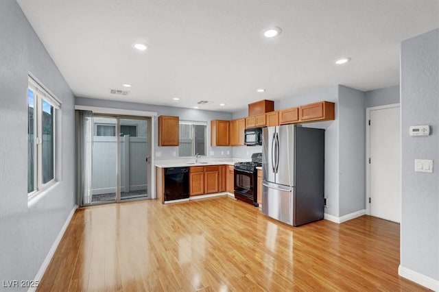 kitchen featuring a sink, black appliances, light countertops, and light wood finished floors