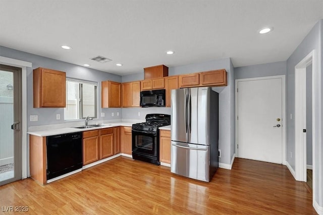 kitchen featuring visible vents, light wood-type flooring, black appliances, a sink, and light countertops