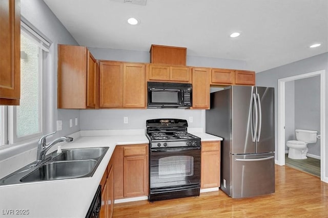 kitchen featuring a healthy amount of sunlight, black appliances, light wood-style floors, and a sink