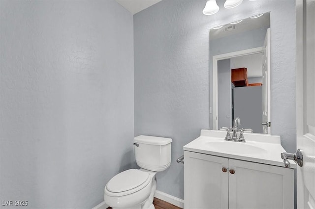 half bath featuring visible vents, toilet, baseboards, vanity, and a textured wall