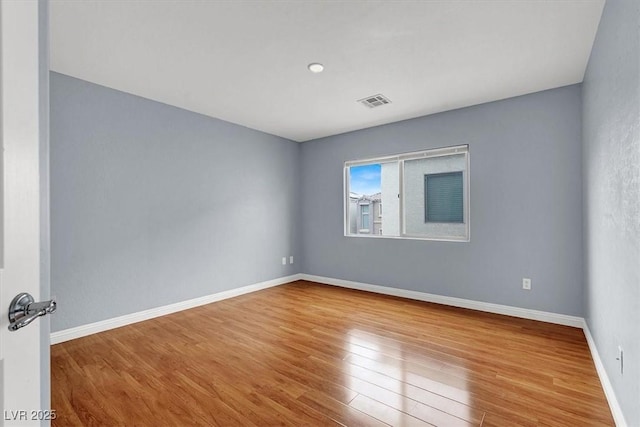 empty room featuring visible vents, wood finished floors, and baseboards