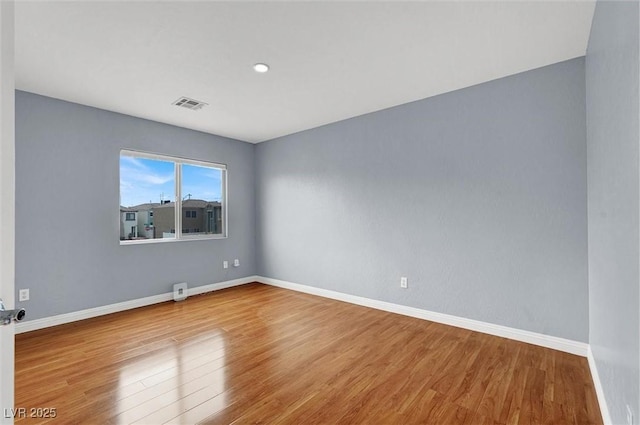 empty room with wood finished floors, visible vents, and baseboards