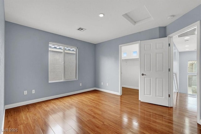 unfurnished room with visible vents, attic access, baseboards, and wood finished floors