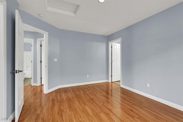 spare room with light wood-type flooring, baseboards, and attic access