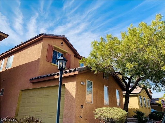 view of side of home featuring stucco siding, a tile roof, and a garage