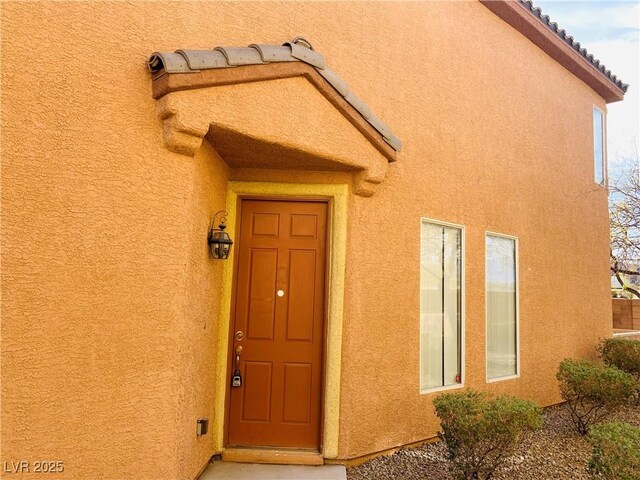 property entrance featuring a tile roof and stucco siding