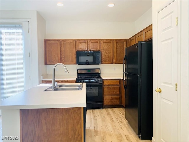 kitchen featuring light countertops, light wood-style flooring, brown cabinets, black appliances, and a sink