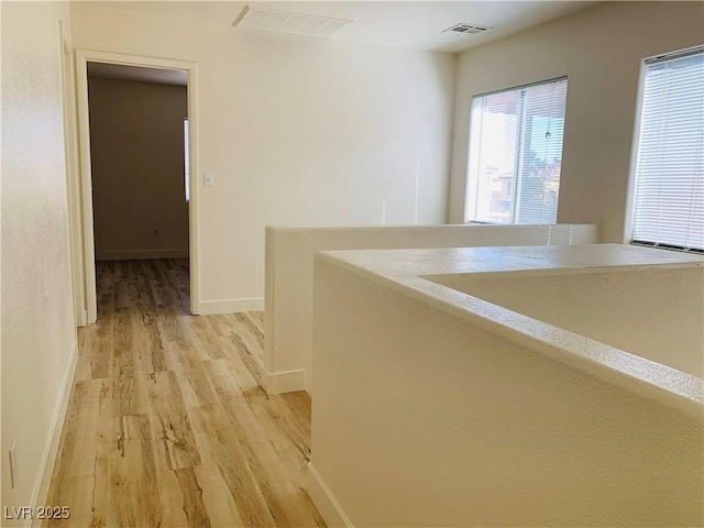 hallway featuring light wood finished floors, visible vents, and baseboards