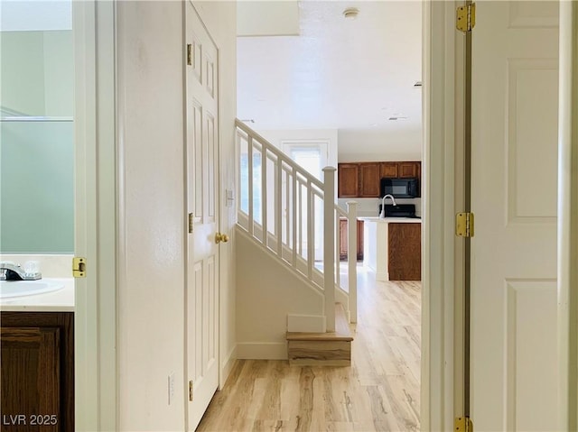 corridor with a sink, light wood-type flooring, baseboards, and stairs