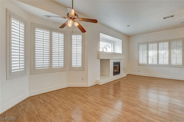 unfurnished living room featuring a ceiling fan, wood finished floors, visible vents, baseboards, and a glass covered fireplace