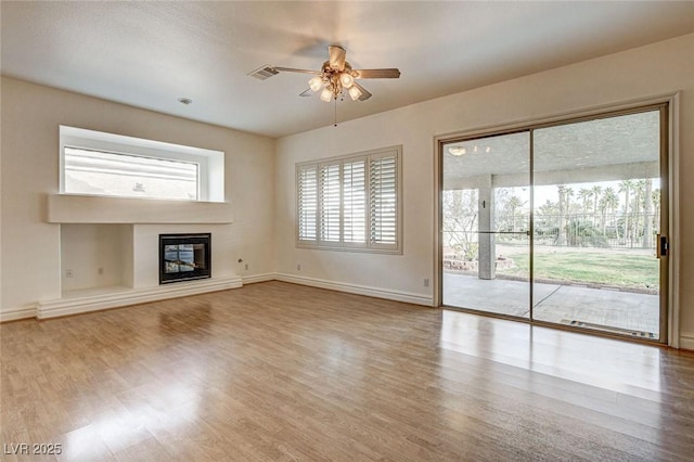 unfurnished living room with a glass covered fireplace, wood finished floors, baseboards, and ceiling fan