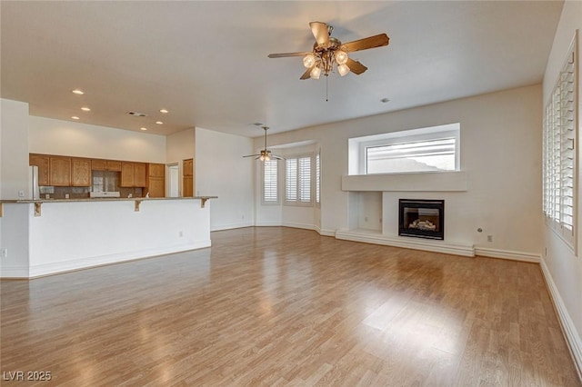 unfurnished living room featuring baseboards, light wood-type flooring, recessed lighting, a glass covered fireplace, and a ceiling fan