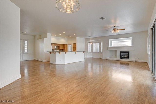 unfurnished living room featuring a glass covered fireplace, visible vents, light wood-type flooring, and baseboards