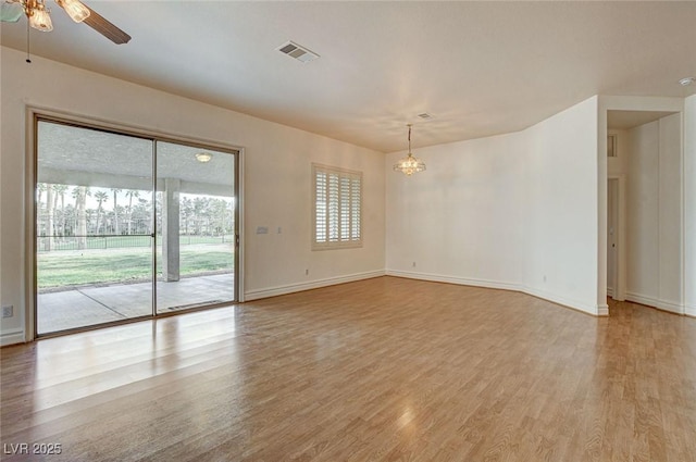 spare room with ceiling fan with notable chandelier, visible vents, light wood finished floors, and baseboards