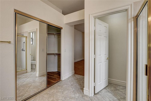 unfurnished bedroom with a closet, baseboards, ensuite bath, and light tile patterned flooring